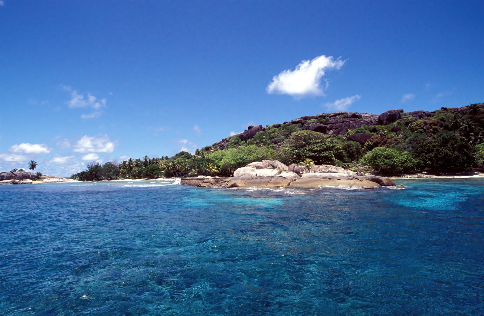 Rocky island fringed with green scrub rising from clear turquoise sea