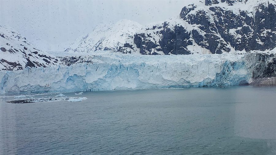 Tidewater glacier meeting a calm Alaskan inlet below snowy peaks