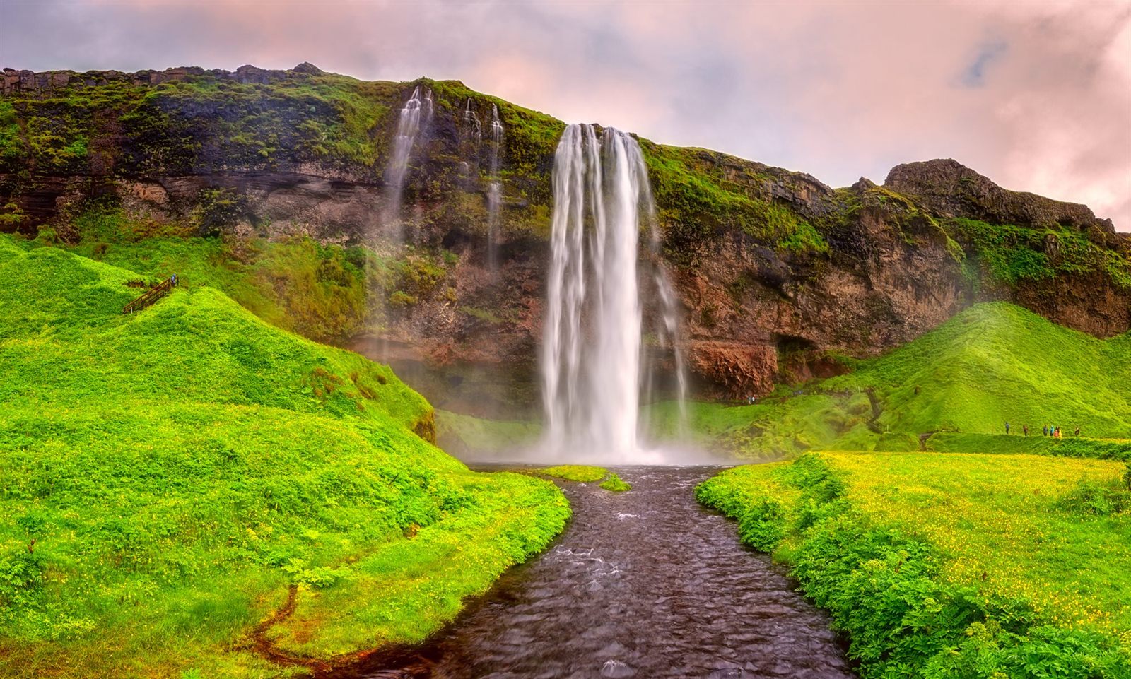 Tall waterfall pouring over a green cliff into a river valley in Iceland